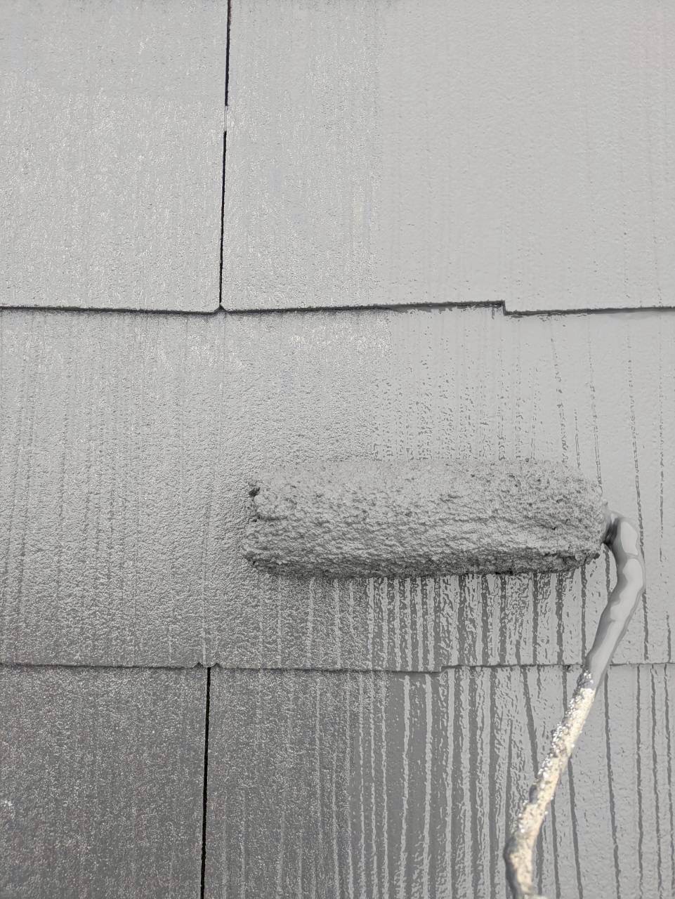 上塗り材で仕上げ塗装中のスレート屋根